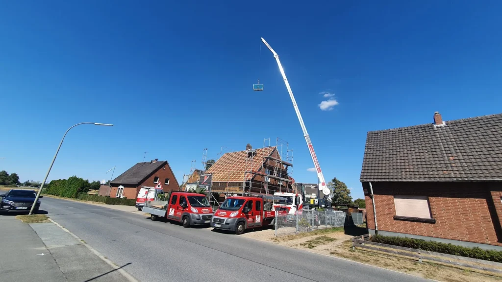 Firmenfahrzeuge von Baumeister und Mobilkran an einer Dachstuhl-Baustelle in einer Wohnstraße