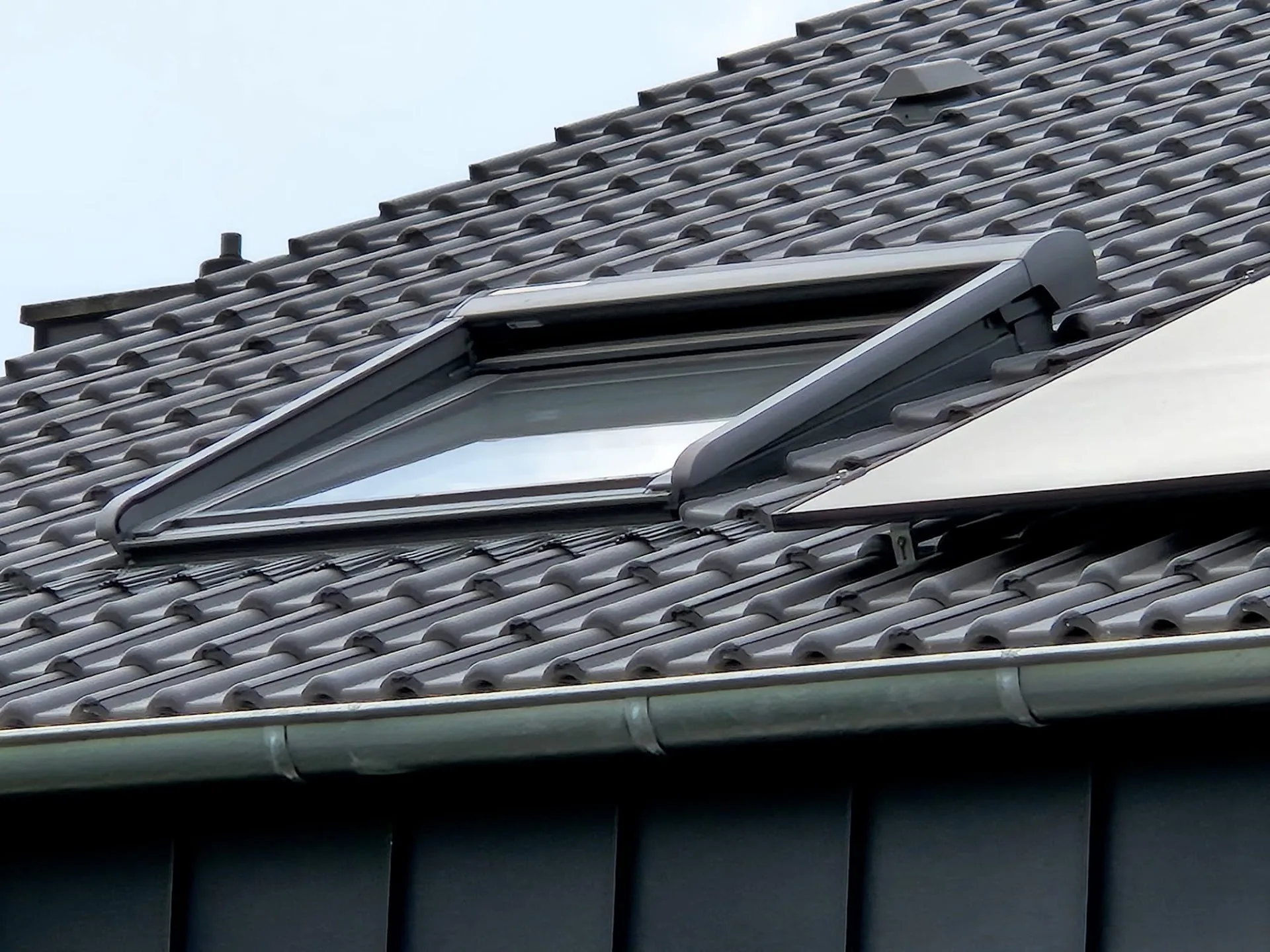 Geöffnetes Dachfenster in neu eingedecktem Steildach mit dunklen Dachsteinen in Goch