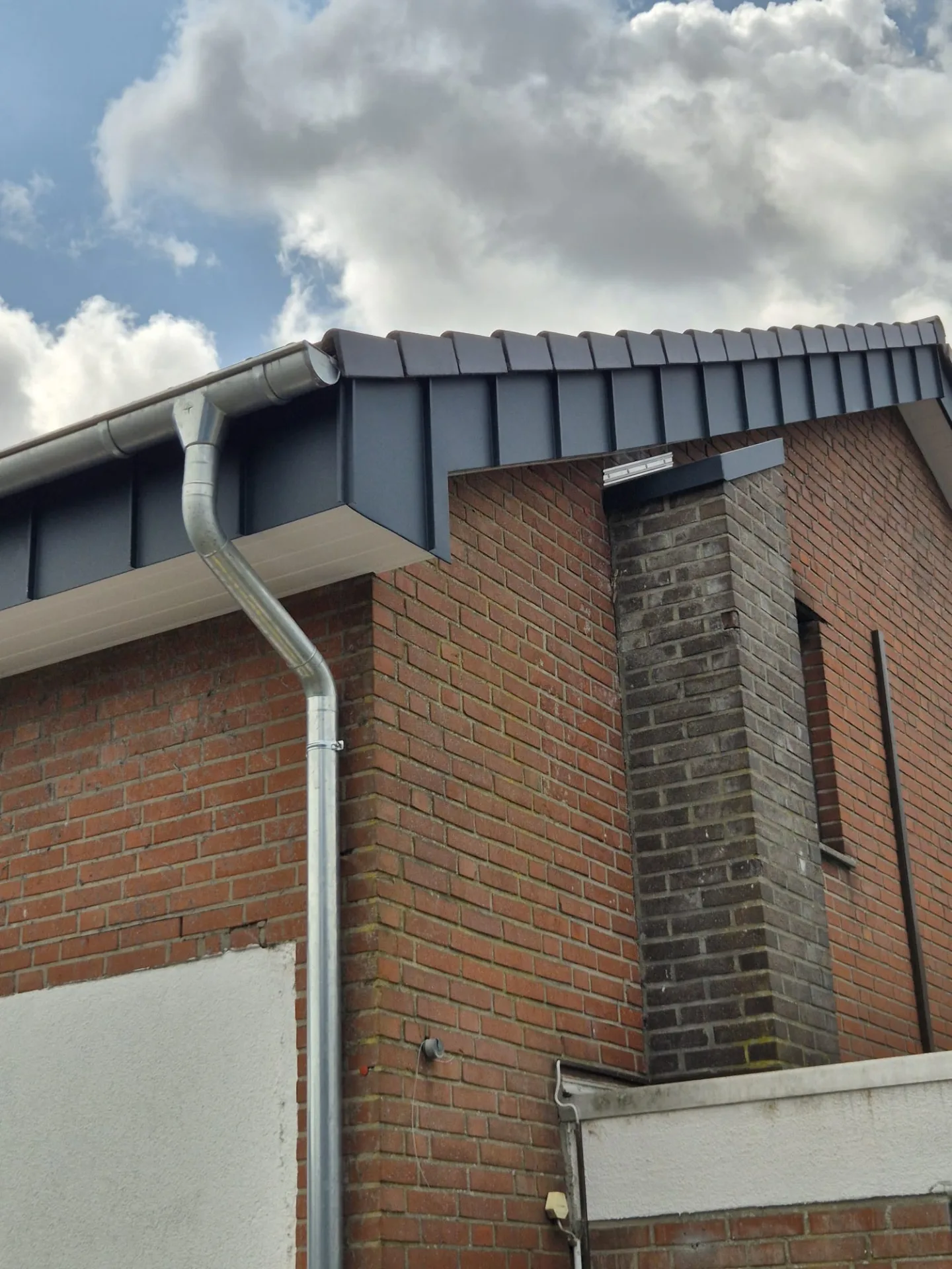 Anthrazitfarbene Stehfalz-Bekleidung am Giebel mit Dachrinne an einem Klinkerhaus in Goch