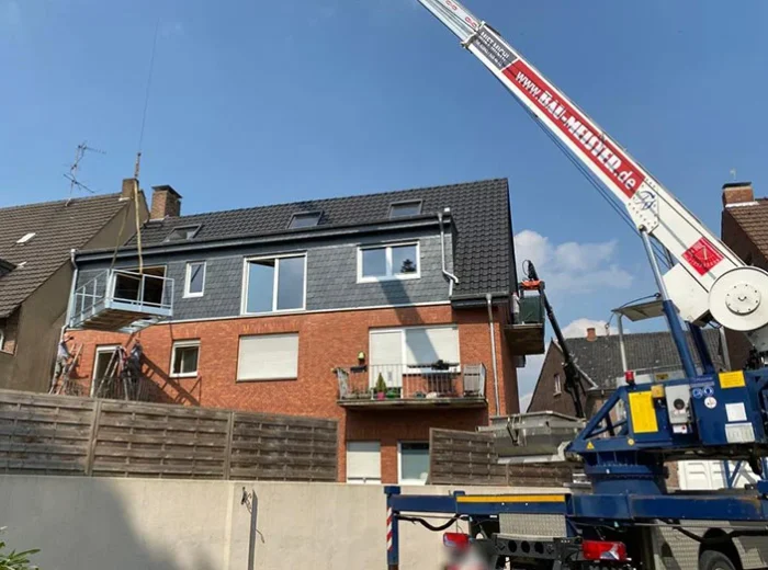 Autokran von Baumeister hebt ein Balkonelement an ein Mehrfamilienhaus