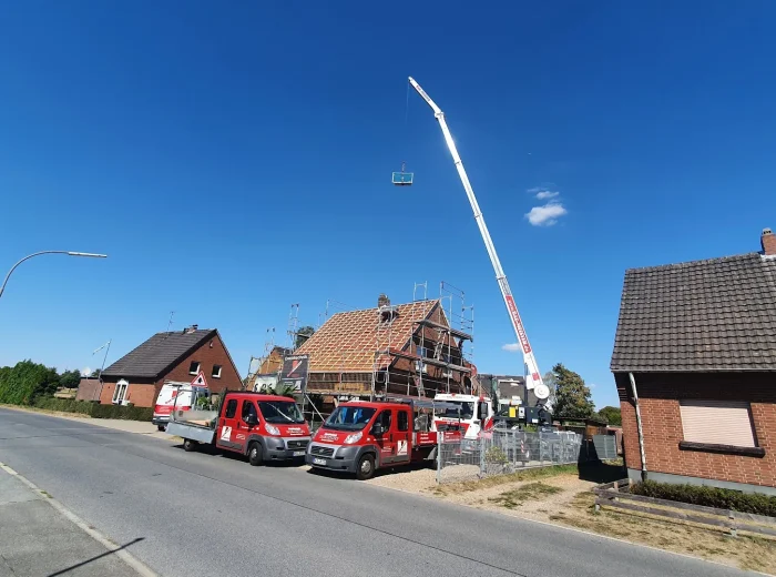 Firmenfahrzeuge von Baumeister und Mobilkran an einer Dachstuhl-Baustelle in einer Wohnstraße