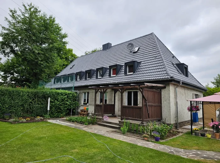 Saniertes Walmdach mit dunklen Dachsteinen und mehreren Gauben an einem Altbau mit Garten