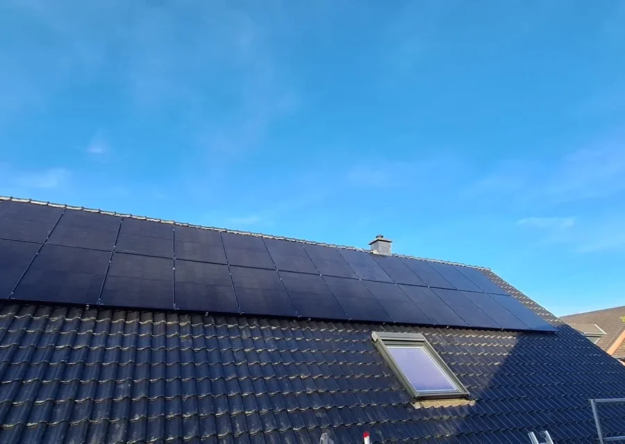 Full-Black-PV-Module und Dachfenster auf dunklem Ziegeldach vor blauem Himmel